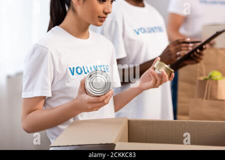 Selektiver Fokus der asiatischen Freiwilligen hält Blechdosen in der Nähe von Pappe Box im Charity Center Stockfoto