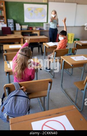 Rückansicht des Mädchens, das ihre Hand in der Klasse hebt In der Schule Stockfoto