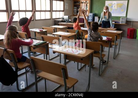 Gruppe von Kindern tragen Gesichtsmasken heben ihre Hände in Die Klasse Stockfoto