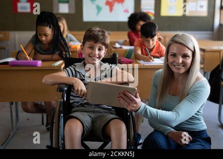 Portrait der Lehrerin und deaktiviert Junge lächelnd während des Sitzens In seinem Rollstuhl in der Klasse Stockfoto