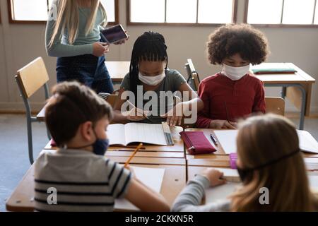 Gruppe von Kindern tragen Gesichtsmasken Studium in der Klasse an Schule Stockfoto