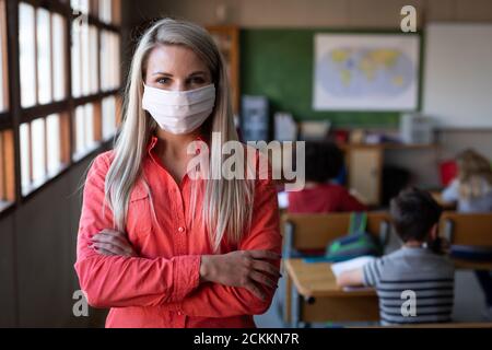 Portrait der Lehrerin mit Gesichtsmaske, die mit ihr steht Arme in der Klasse gekreuzt Stockfoto