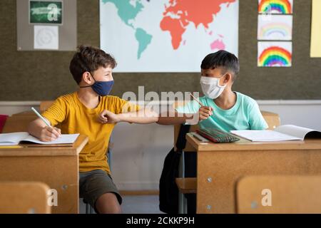 Zwei Jungen mit Gesichtsmasken begrüßen sich gegenseitig durch Berühren Ellbogen in der Schule Stockfoto