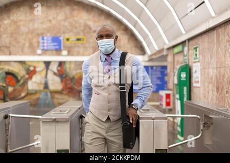 Eleganter schwarzer Mann, der aus einer U-Bahn-Station läuft. Er trägt eine Gesichtsmaske. Konzept der Rückkehr zur Arbeit nach der Einengung. Stockfoto