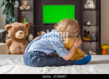 Netter kleiner Junge und sein Teddybär beim Fernsehen sitzen Auf einer Couch im Wohnzimmer zu Hause Stockfoto