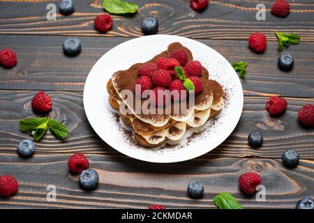 Portion Classic Tiramisu Dessert mit Himbeeren und Heidelbeeren auf Holzhintergrund Stockfoto