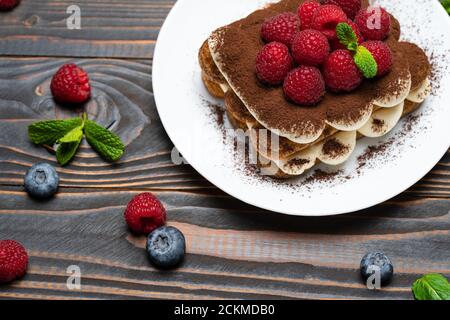 Portion Classic Tiramisu Dessert mit Himbeeren und Heidelbeeren auf Holzhintergrund Stockfoto