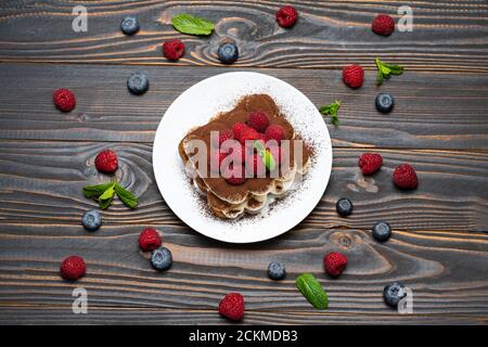 Portion Classic Tiramisu Dessert mit Himbeeren und Heidelbeeren auf Holzhintergrund Stockfoto