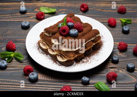 Portion Classic Tiramisu Dessert mit Himbeeren und Heidelbeeren auf Holzhintergrund Stockfoto