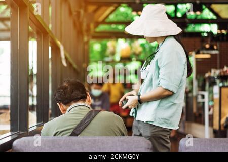 Rückansicht des asiatischen männlichen Kunden sitzen in Warteschleife sozialen Abstand Schlange für Take Away Drink im Café. Neues normales Lifestyle-Konzept. Stockfoto