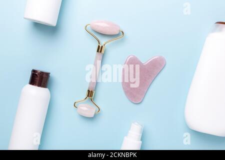 Gua Sha Massagegerät, Gesichtswalze und Kosmetikflaschen auf blauem Hintergrund. Massage-Tool für Gesichtshaut Pflege, SPA Beauty-Behandlung Konzept - Bild Stockfoto