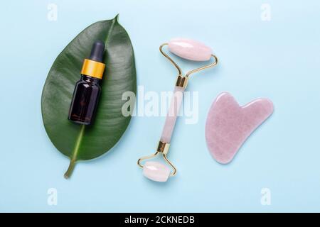 Kosmetikflaschen, Gesichtsserum, Gesichtsmassageroller und Gua Sha Massagegerät auf blauem Hintergrund. Anti-Age-, Lifting- und Toning-Behandlung zu Hause - Bild Stockfoto