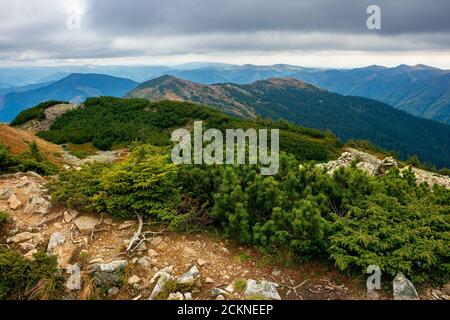 Blick von der Spitze eines Berges. wolkige Herbstlandschaft. Bergkette hinter dem Tal in der Ferne. Dramatisches Wetter in farbenfroher Landschaft Stockfoto