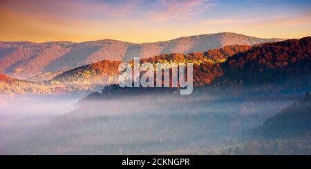 Berglandschaft im Herbst. Nebel glüht im Morgenlicht. Dramatischer Himmel mit Wolken bei Sonnenaufgang Stockfoto