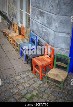 Ein Stillleben von bunten Kinderstühlen aus Holz, alle in einer Reihe auf einer Straße. Stockfoto