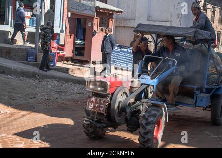 Bhaktapur, Kathmandu, Nepal - 23. Dezember 2019: Drei nicht identifizierte Arbeiter transportieren Ladung per Traktor neben vier weiteren nicht identifizierten Personen Stockfoto