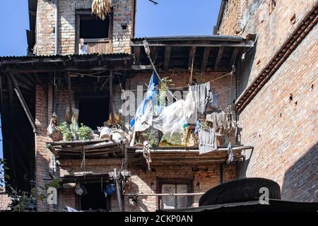 Blick auf die Straße von ein paar einfachen Balkonen aus Bambus mit Pflanzen, Kunststoff und Wäsche auf einem Backsteingebäude in Bhaktapur, Kathmandu, Nepal Stockfoto