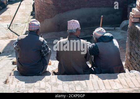 Bhaktapur, Kathmandu, Nepal - 23. Dezember 2019: Am 23. Dezember 2019 sitzen drei unbekannte Männer auf der Straßenseite und sprechen über eine Treppe Stockfoto