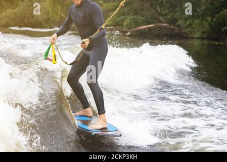 Unkenntlich fit kaukasischen Mann reitet wecken Brandung auf Fluss oder See am Abend in der untergehenden Sonne. Konzept für Wassersport, Urlaub und Wochenendaktivitäten. Stockfoto