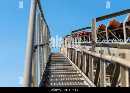 Nahaufnahme des Förderbandes im Betonwerk mit Transportrollen, sichtbaren Metalltreppen und Geländern. Stockfoto