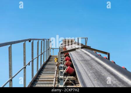 Nahaufnahme des Förderbandes im Betonwerk mit Transportrollen, sichtbaren Metalltreppen und Geländern. Stockfoto