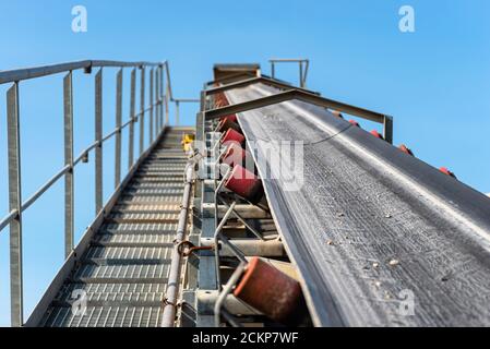 Nahaufnahme des Förderbandes im Betonwerk mit Transportrollen, sichtbaren Metalltreppen und Geländern. Stockfoto