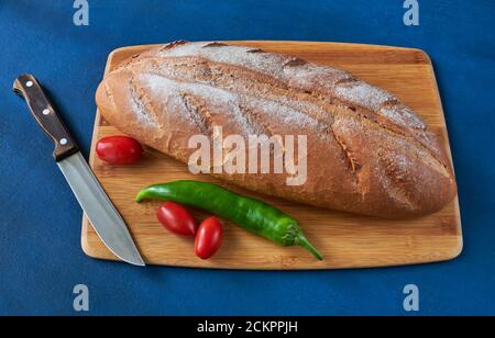 Brot, Tomaten, Chili und ein Messer liegen auf dem Schneidebrett, geringe Schärfentiefe, Stillleben Stockfoto