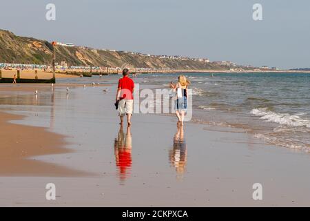 Boscombe, Bournemouth, Dorset, UK, 16. September 2020, Wetter. Menschen am Strand und im Meer genießen den dritten Tag der September Hitzewelle mit heißem Sonnenschein am Nachmittag. Ein Paar geht am Ufer entlang auf nassem Sand. Kredit: Paul Biggins/Alamy Live Nachrichten Stockfoto