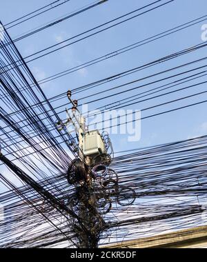 Die Kommunikationskabel (Internet, Telefon, etc.) sind am elektrischen Pol unter der Transformatoreneinheit, einem städtischen Gebiet in der Nähe des Geschäfts verwickelt Stockfoto