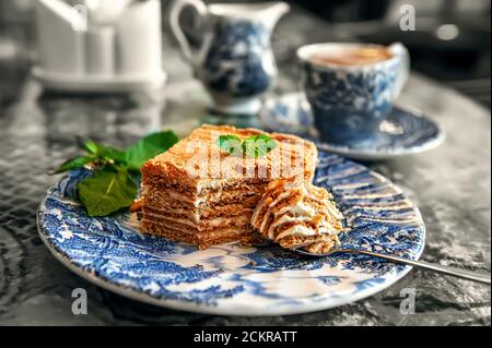 Geschichtetes Stück Honigkuchen auf einem antiken Teller. Nahaufnahme eines leckeren Honigkuchens mit Minze Stockfoto