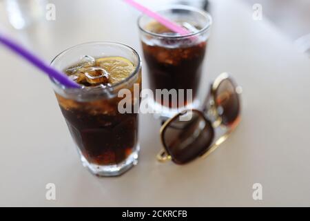 Zwei volle Strohgläser und Sonnenbrillen stehen auf weißem Tisch. Stockfoto