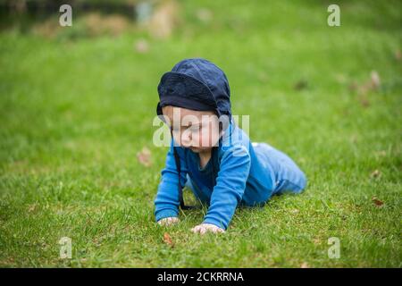 6 Monate altes Baby kriecht draußen im grünen Gras Stockfoto