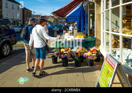 Die High Street der Marktstadt Stokesley North Yorkshire an einem sonnigen Herbsttag Shopper Blick auf Blumen Zum Verkauf Stockfoto