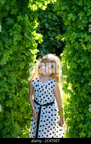 Schöne blonde Mädchen in gepunkteten Kleid unter grünen Blättern Stockfoto