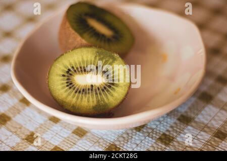 Ein Kiwi in einer Schüssel auf einem in die Hälfte geschnitten Karierte Tischdecke Stockfoto