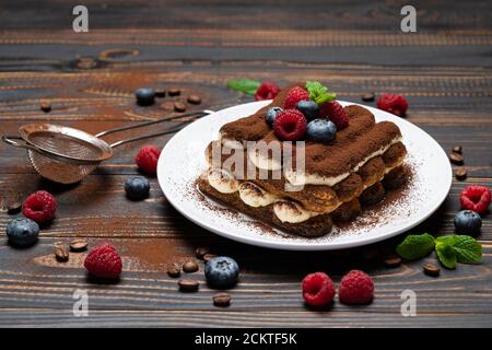 Portion Classic Tiramisu Dessert mit Himbeeren und Heidelbeeren auf Holzhintergrund Stockfoto