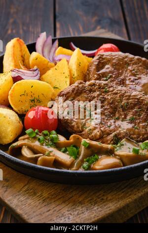 Nahaufnahme der Pfanne mit gebratenem Schweinefilet, Kartoffelkeilen, Pilzen und Tomaten Stockfoto