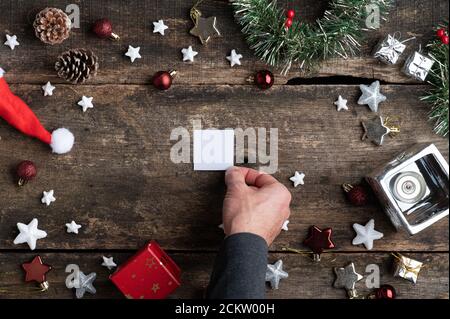 Top view of male hand placing a small blank piece of paper in the center of holiday setting full of christmas ornaments. Stockfoto