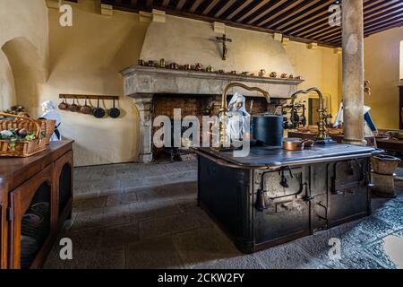 Ein Kruzifix hängt über dem Steinofen der Klosterküche im Museum des Hôtel-Dieu in Beaune, Burgund, Frankreich. Kupferntöpfe säumen den Kaminsims und Pfannen hängen an einem Holzgestell an der Wand. Ein Korb mit Gemüse steht links auf der Anrichte, und der schwarze Gusseisenofen nimmt die Mitte des Raumes ein. Kanzler Nicolas Rolin gründete das Hôtel-Dieu 1443 als Krankenhaus für die Armen, und es versorgte Patienten bis 1971. Stockfoto