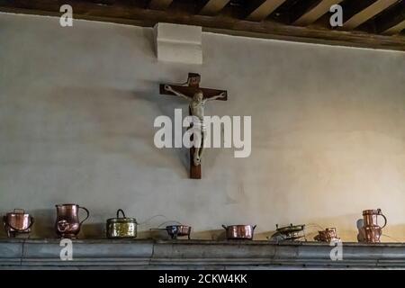 Ein christliches Kreuz hängt über einem Kaminsims voller Kupferschiffe im Hotel-Dieu, Beaune, Frankreich Stockfoto