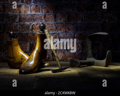 Paar Vintage Holz Schuster Schuh reicht, Messing Gewichte, Parafin Lampe traditionellen Hammer mit WWII Brust Backstein Wand im Hintergrund dramatische Beleuchtung Stockfoto