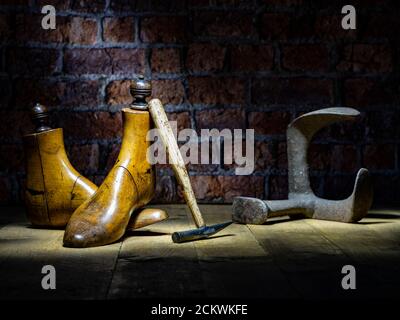 Paar Vintage Holz Schuster Schuh reicht, Messing Gewichte, Parafin Lampe traditionellen Hammer mit WWII Brust Backstein Wand im Hintergrund dramatische Beleuchtung Stockfoto