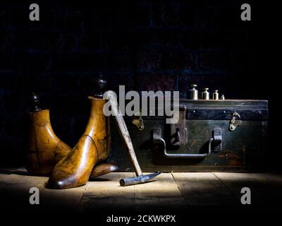 Paar Vintage Holz Schuster Schuh reicht, Messing Gewichte, Parafin Lampe traditionellen Hammer mit WWII Brust Backstein Wand im Hintergrund dramatische Beleuchtung Stockfoto