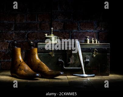 Paar Vintage Holz Schuster Schuh reicht, Messing Gewichte, Parafin Lampe traditionellen Hammer mit WWII Brust Backstein Wand im Hintergrund dramatische Beleuchtung Stockfoto