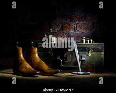 Paar Vintage Holz Schuster Schuh reicht, Messing Gewichte, Parafin Lampe traditionellen Hammer mit WWII Brust Backstein Wand im Hintergrund dramatische Beleuchtung Stockfoto