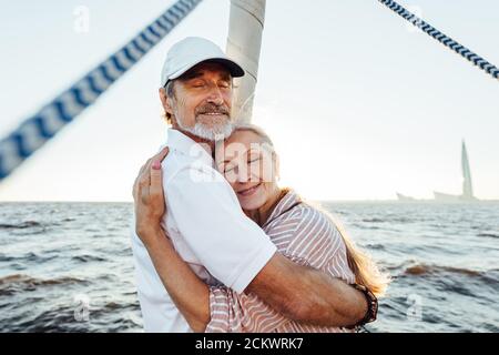 Glückliche ältere Menschen umarmen sich gegenseitig und genießen einen Sonnenuntergang auf dem Segelboot. Schöne reife Paar umarmt im Freien. Stockfoto