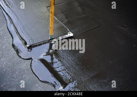 Mann versiegelt Asphalteinfahrt/Sealcoating Stockfoto