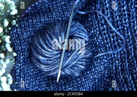 Nadelarbeit und ein Bouquet von weißen Blumen. Textur schöner blauer Strickstoff mit metallischen Fasern und Stricknadeln und Klau als Hintergrund Stockfoto