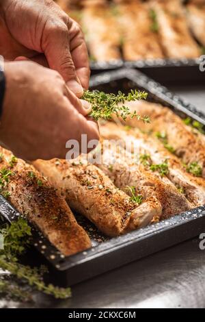 Koch in der Küche bereitet Schweinefilets in einer Backform Und verwendet Kräuter Stockfoto