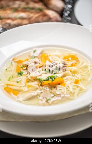 Hühnersuppe auf einem Teller mit Nudeln, Karotten und frischer Petersilie darauf Stockfoto